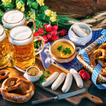 Bavarian sausages with pretzels, sweet mustard and beer mugs on rustic wooden table. Oktoberfest menu