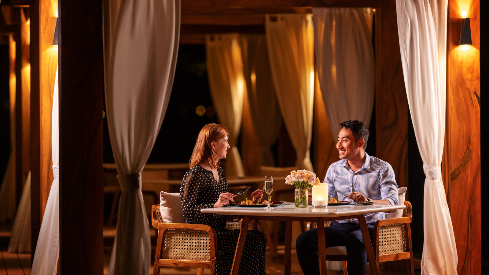 Two people having a romantic dinner by the beach at Tropicana Beach Club's cabana inside Mövenpick Resort Cam Ranh.