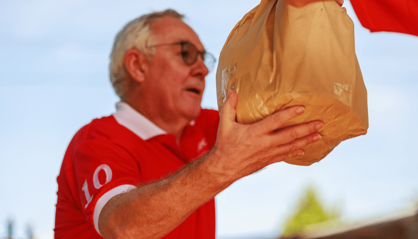 an old man in red t-shirt receives a bag.